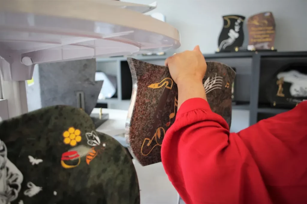 Détail d'une main tenant une plaque funéraire en granit gravée d'une portée.