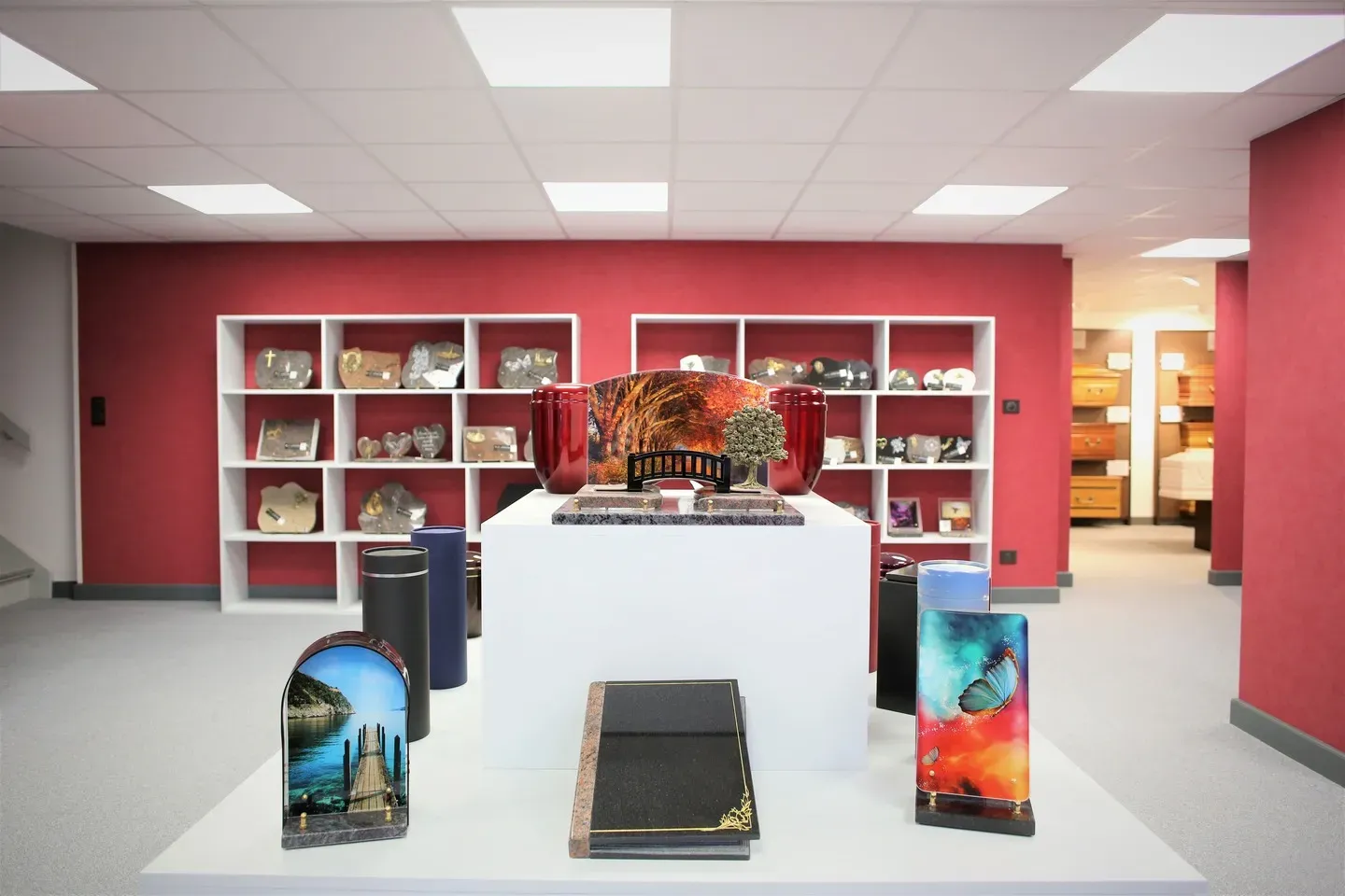 Articles funéraires, plaques et urnes exposés devant un mur rouge.