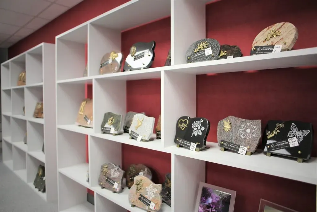 Étagères blanches exposant des plaques funéraires gravées avec motifs.